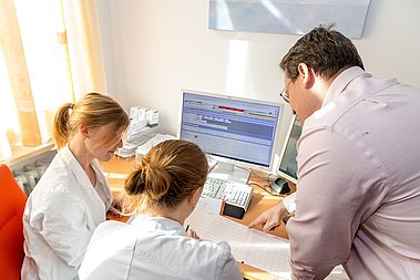 Drei Ärzte sitzen gemeinsam vor einem Computer und beurteilen ein Dokument. 