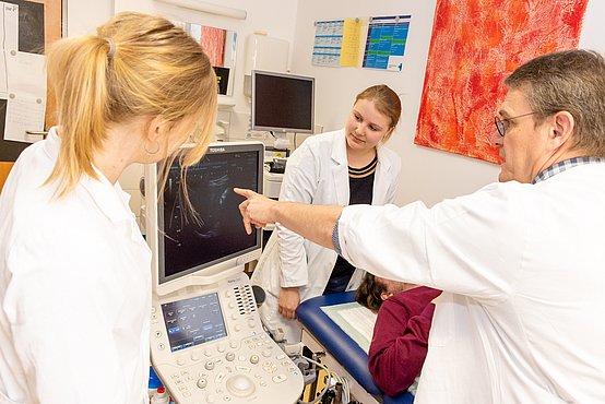 Ein Patient mit einer Tumorerkrankung wird bei einem Ultraschall von mehreren Ärzten untersucht.