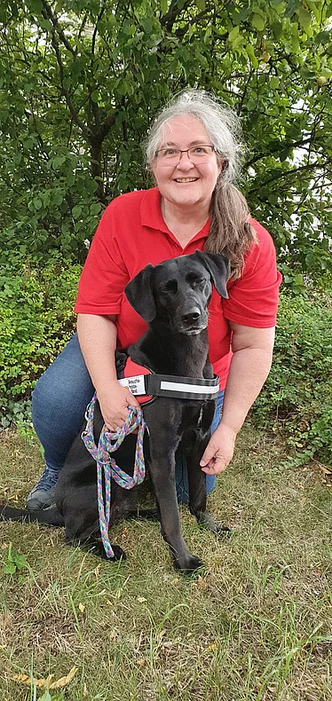 Juliane Müller mit dem Besuchshund Flicka.png Janine Müller sitzt mit dem Besuchshund Flicka im Grünen.