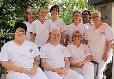 Pflegeteam.png Das Pflegeteam steht und sitzt im freien aufgereiht und lächelt in die Kamera.