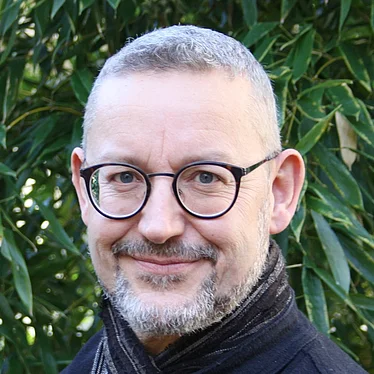 Musiktherapeut Andre Hartinger im freien und in die Kamera lächelnd.