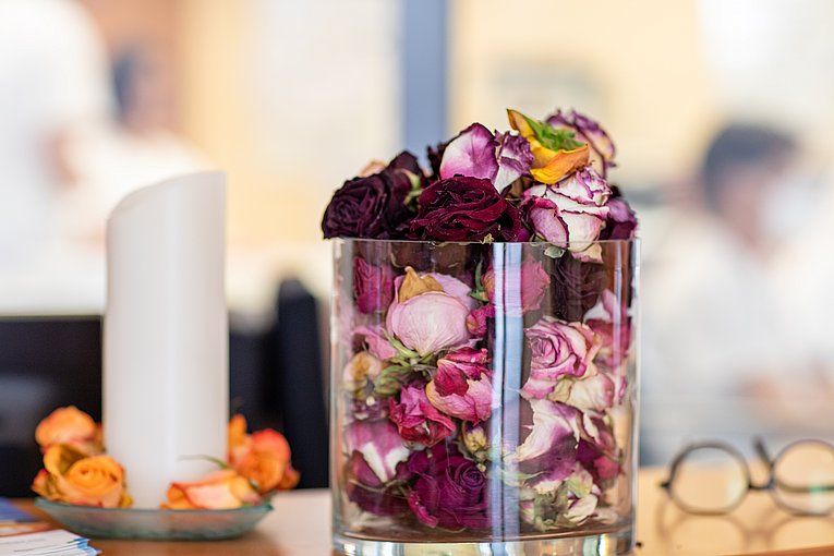 Links steht eine weiße Kerze. Rechts daneben ein großes Glas mit getrockneten Rosenköpfen.